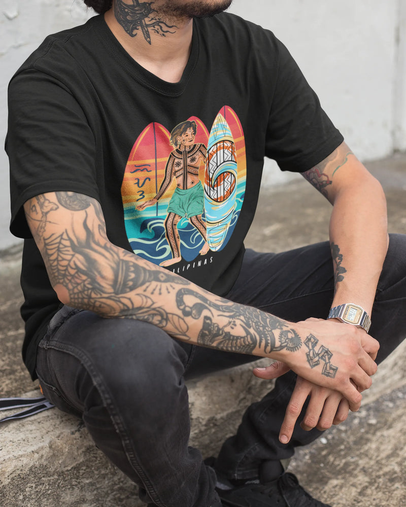 Closeup of a tattooed man sitting down in the black Surfin' Siargao badlit suwat Bisaya t-shirt