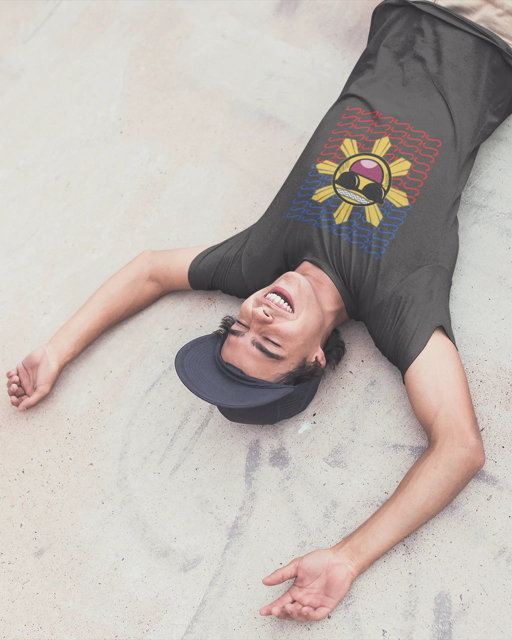 Pinoy skater laughing on the ground in a Baybayin t-shirt, playful filipino streetwear brand energy.