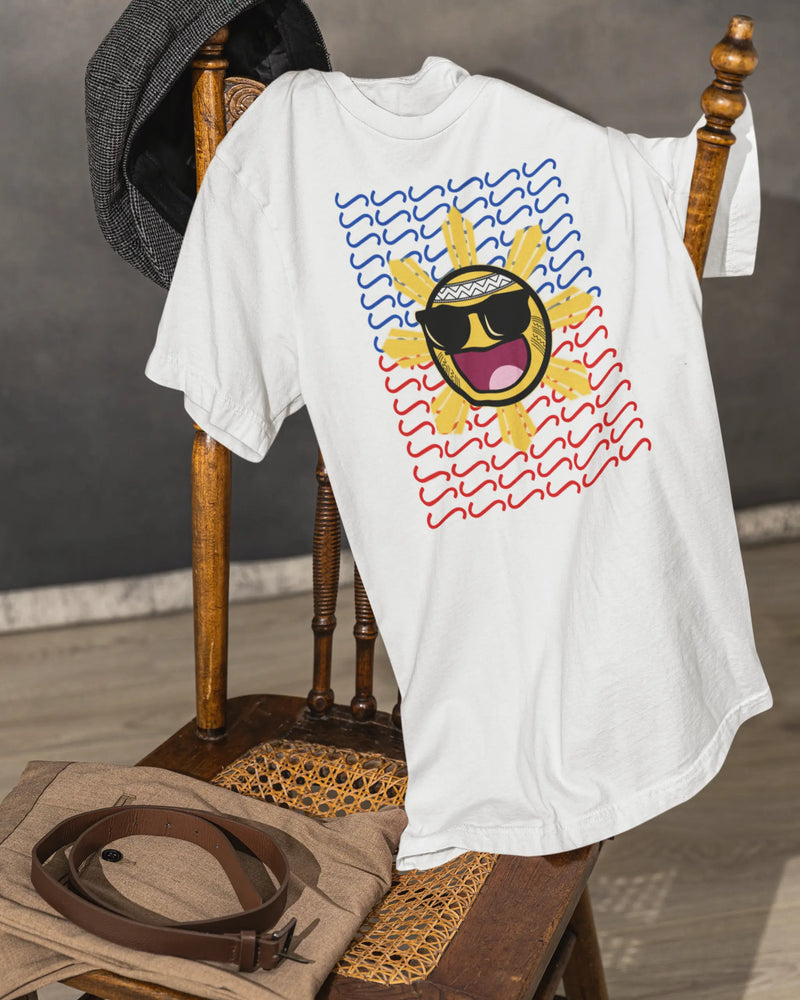 White Baybayin t-shirt draped on a vintage chair, clean filipino streetwear with the sun graphic.